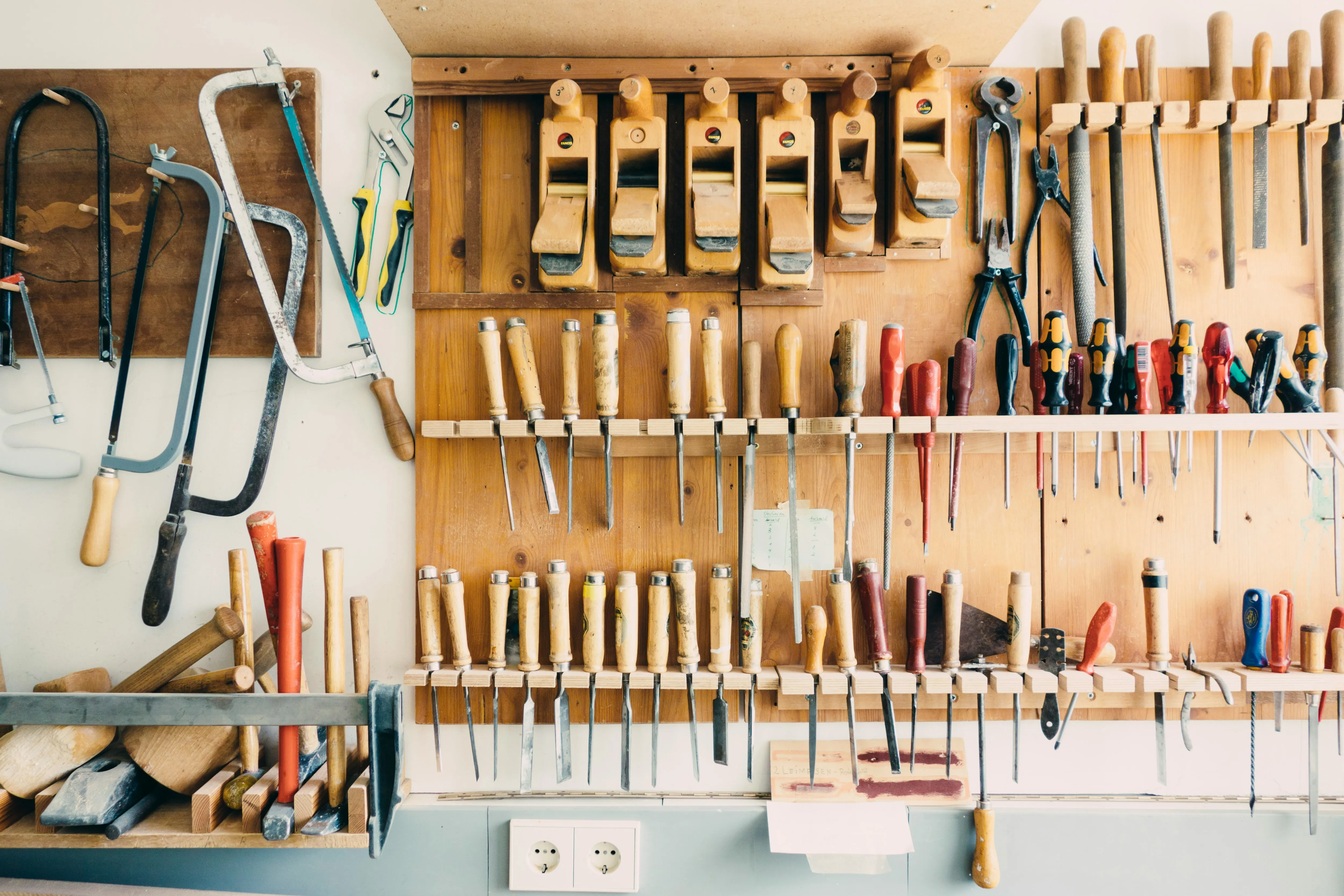 A pegboard lined with woodworking hand tools — planes, chisels, and files, each in its place.