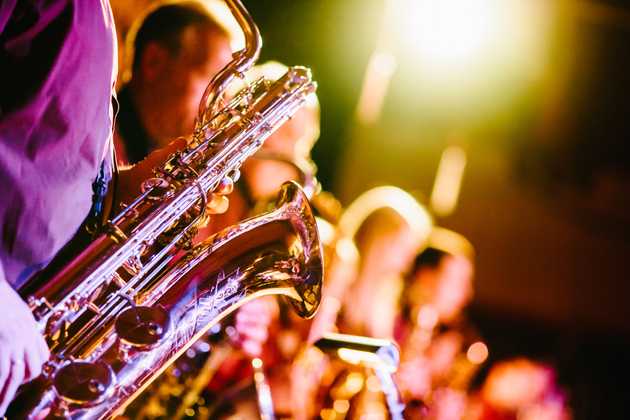 Image of a saxophone with a group of jazz musicians in the background.